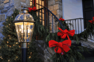 Eco-friendly holiday landscaping with LED string lights on evergreen garland, natural wreaths with red bows, and energy-efficient lantern at commercial property entrance